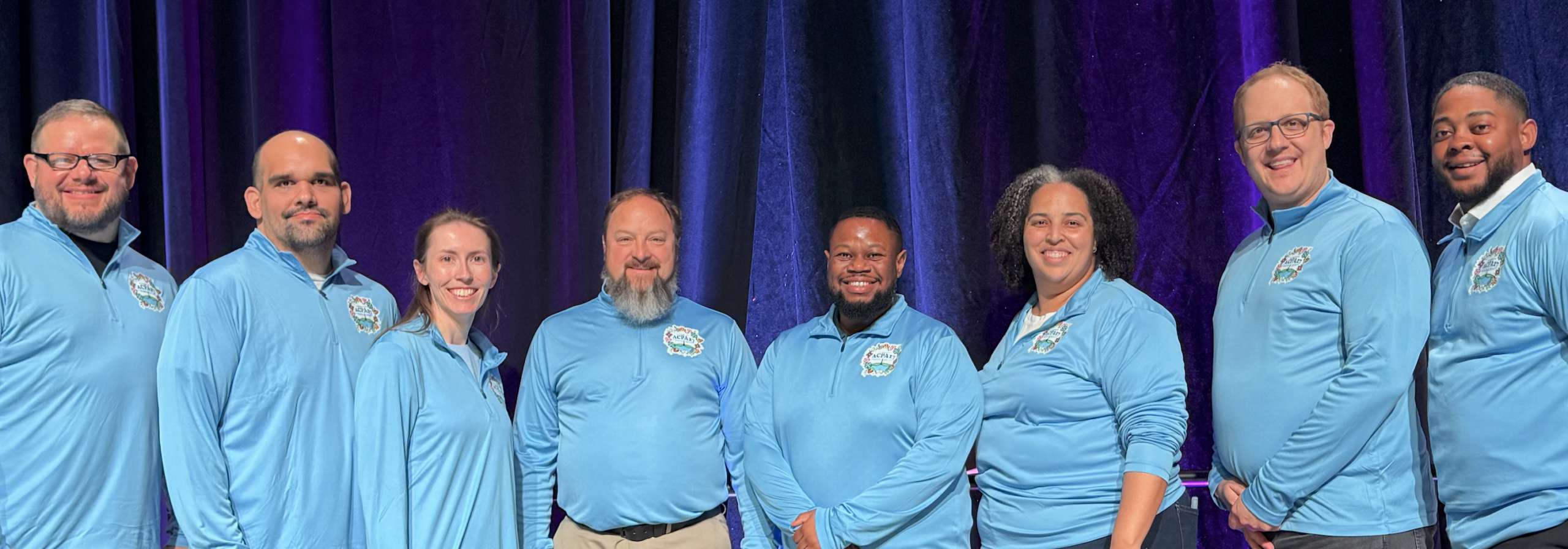 group photo of the ACPA27 steering team all wearing matching sky blue shirts and smiling at the camera
